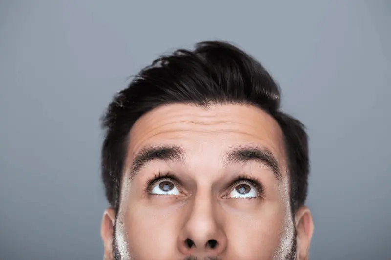 A man's close-up, gazing upward, exudes confidence for a blog post on camera confidence.